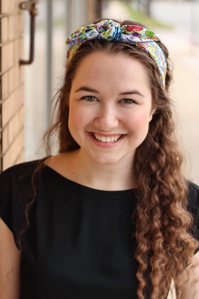 A Smiling Headshot of Jessica Jama wearing a Black Shirt and Colorful Bow